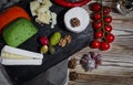 Mix cheese on dark background on wood board with grapes, honey, nuts, tomatoes and basil. Top view Royalty Free Stock Photo