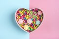 Mix colorful chocolate sweets lie in gift box shape of heart on blue, pink background Royalty Free Stock Photo
