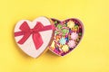 Mix colorful chocolate sweets lie in gift box shape of heart on yellow background Flat lay Royalty Free Stock Photo