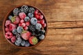 Mix of different frozen berries in bowl on wooden table, top view. Space for text