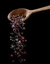 Mix of different peppercorns and salt falling down from the wooden spoon at black background Royalty Free Stock Photo