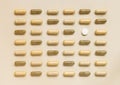 Mix of medical capsules with onewhite pill in lines on light beige top view. Dietary supplements Royalty Free Stock Photo