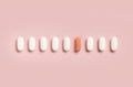 Mix of medical pills with one pink capsule in a line on light pink top view. Dietary supplements Royalty Free Stock Photo