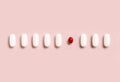 Mix of medical pills with one red capsule in a line on light pink top view. Dietary supplements Royalty Free Stock Photo