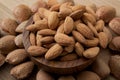 Mix of shelled and unshelled nuts with close up on an almond bowl made of wood with a heap of almonds still in shell surrounding