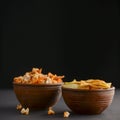 Mix of snacks in bowls: salty butter popcorn and tortilla chips in ceramic bowl over dark black background. Royalty Free Stock Photo