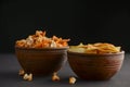 Mix of snacks in bowls: salty butter popcorn and tortilla chips in ceramic bowl over dark black background. Royalty Free Stock Photo