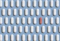 Mix of white medical pills in a line with one pink on light blue top view. Dietary supplements Royalty Free Stock Photo