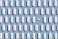 Mix of white medical pills in a line with one yellow on light blue top view. Dietary supplements Royalty Free Stock Photo