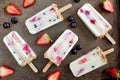 Mixed berry yogurt popsicles with granola over a dark background
