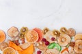 Mixed dried fruit and vegetable chips, candied pumpkin slices, nuts and seeds on white marble background Royalty Free Stock Photo