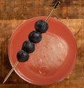 Mixed drink cocktail with four blueberries and square ice cube with a wooden background