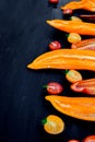 Mixed of half red and yellow pepper with a green branch near cherry tomato on black backround. Top view. Frame. Copy space. Royalty Free Stock Photo