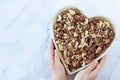 Mixed nuts (hazelnut, almond, walnut, Brazil, and pine nuts) in a heart-shaped dish with female hands isolated on white