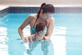 Mixed race asian mother training teaching her newborn baby to float in swimming pool Royalty Free Stock Photo