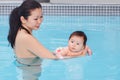 Mixed race asian mother training teaching her newborn baby to float in swimming pool Royalty Free Stock Photo