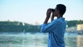 Mixed-race boy looking through binoculars at boats on river, teenager dreams