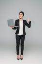 Mixed race businesswoman holding laptop and showing thumb up on grey background Royalty Free Stock Photo