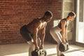 Mixed-race couple doing squats exercise, while holding in hands heavy sandbags. Royalty Free Stock Photo