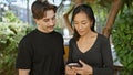 A mixed-race couple, man and woman, engage with a smartphone in a lush outdoor park setting