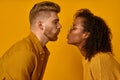 Mixed race couple stand in profile, keep lips folded, staring at each other, going to kiss, dressed casual mustard color Royalty Free Stock Photo