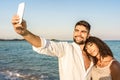 Mixed race couple in vacation at sea resort making a self portrait at sunset or dawn - Handsome smiling bearded man take photo Royalty Free Stock Photo