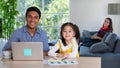 Mixed race family sharing time in living room. Caucasian father using notebook computer to work and half-Thai girl standing beside Royalty Free Stock Photo