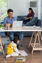 Mixed race family sharing time in living room. Caucasian father using notebook computer to work and half-Thai playing and painting Royalty Free Stock Photo