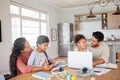 Mixed race family sitting together doing homework and using digital devices at kitchen table. Couple sitting at home Royalty Free Stock Photo