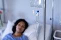 Mixed race female patient lying asleep in hospital bed hooked up to iv drip, selective focus Royalty Free Stock Photo