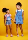 Mixed race girl sisters holding hands isolated against a yellow background. Cute hispanic children posing inside. Happy Royalty Free Stock Photo