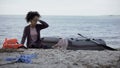 Mixed race girl sitting on beach near boat, flood disaster victim, shipwreck
