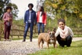 Mixed race girl squatting to pet her dog during a family walk in the countryside looking to camera, low angle