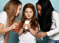 Mixed race girls friends in jeans and white t-shirts standing with glasses of water, milk and juice and looking at milk