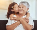 Mixed race granddaughter kissing grandmothers cheek in living room at home. Senior woman enjoying weekend with adorable Royalty Free Stock Photo