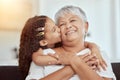 Mixed race granddaughter kissing grandmothers cheek in living room at home. Senior woman enjoying weekend with adorable Royalty Free Stock Photo