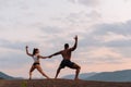 Mixed race gymnastic couple with perfect bodies in sportswear dancing on mountains landscape background. Pink sunset sky Royalty Free Stock Photo