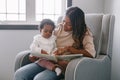 Mixed race Indian mom reading book with African black baby girl toddler at home. Early age children education and development. Royalty Free Stock Photo