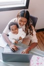 Mixed race Indian mother with African black baby working online from home on Internet. Workplace of freelancer woman with kid. Royalty Free Stock Photo