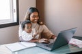 Mixed race Indian mother with African black baby working online from home on Internet. Workplace of freelancer woman with kid. Royalty Free Stock Photo