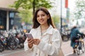 Mixed-race LGBT proud and confident Turkish young woman holding a phone in the street smiling wearing white casual