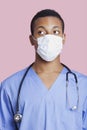 Mixed race male surgeon wearing surgical mask over pink background