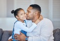 Mixed race man kissing his adorable little daughter on the cheek while bonding together at home. Small girl feeling