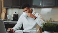 Mixed-race man speaking by smartphone and working on computer at home kitchen