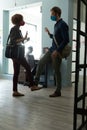 Mixed race man and woman wearing masks greeting with feet in office