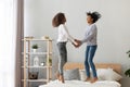 Black mother and adolescent daughter holding hands jumping on bed Royalty Free Stock Photo