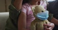 Mixed race mother and daughter hugging,daughter holding tedy bear with face mask