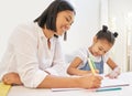 Mixed race mother helping her daughter with her homework. Mom teaching daughter to read and write during homeschool Royalty Free Stock Photo