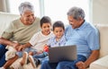 Mixed race senior couple bonding with their grandsons and using a laptop on the sofa at home. Hispanic senior man and Royalty Free Stock Photo