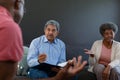 Mixed race senior male counsellor with clipboard advising diverse group of senior friends Royalty Free Stock Photo